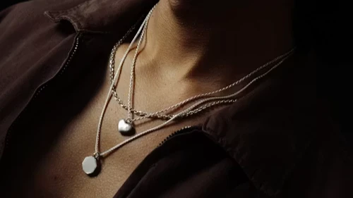 A Person Wearing Layered Silver Necklaces With Pendants
