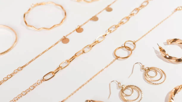Collection of elegant gold-plated jewelry including bracelets, necklaces, and earrings arranged on a white surface.