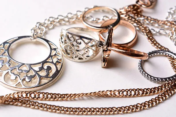 A collection of silver and gold jewelry including filigree rings, a pendant, and chains on a white surface.